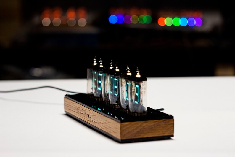 May include: A wooden clock with six Nixie tubes displaying the time in a bright blue-green colour. The clock is on a white surface.