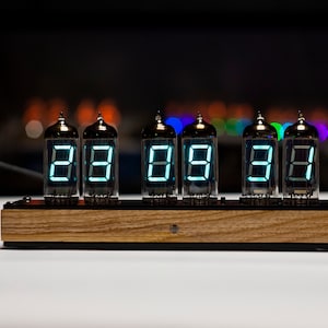 May include: A vintage-style clock with six Nixie tubes displaying the time as 88:88:88. The clock has a wooden base and is lit with a bright blue-green light.