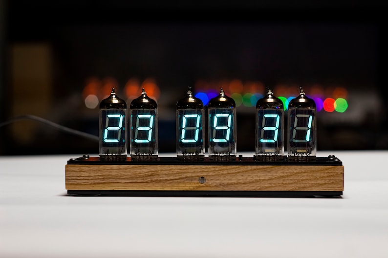 May include: A vintage-style clock with six Nixie tubes displaying the time as 88:88:88. The clock has a wooden base and is lit with a bright blue-green light.