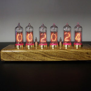 May include: A wooden clock with six clear glass tubes displaying the time as 00:02:04. The tubes are lit with a warm orange glow and have a pink hue at the bottom.