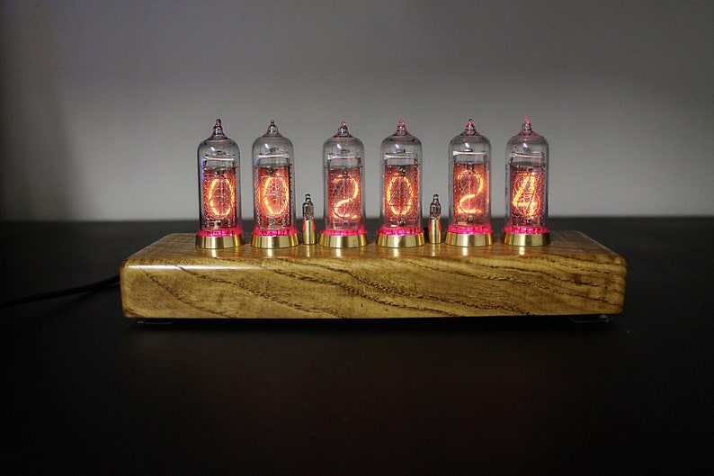 May include: A wooden clock with six clear glass tubes displaying the time as 00:02:04. The tubes are lit with a warm orange glow and have a pink hue at the bottom.
