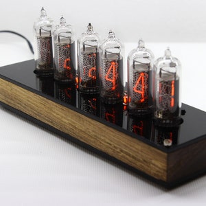May include: A wooden clock with six red glowing Nixie tubes displaying the time 5:44. The clock has a black acrylic face and a wooden base.