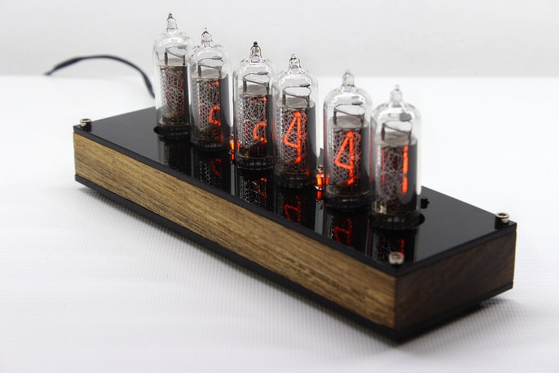 May include: A wooden clock with six red glowing Nixie tubes displaying the time 5:44. The clock has a black acrylic face and a wooden base.
