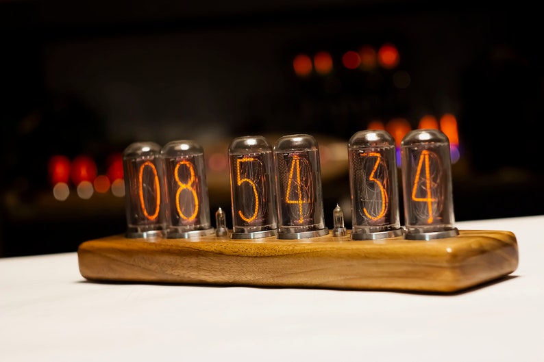 Puede incluir: Un reloj de madera con cuatro tubos Nixie que muestran la hora 08:54:34. Los tubos est&aacute;n iluminados con un brillo naranja.