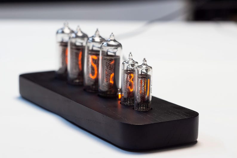 K&ouml;nnte beinhalten: Eine Digitaluhr mit sechs Glasr&ouml;hren, die orangefarbene Ziffern anzeigen. Die R&ouml;hren sind auf einem schwarzen Holzsockel montiert. Die Uhr ist ein elektronisches Ger&auml;t im Retro-Stil.