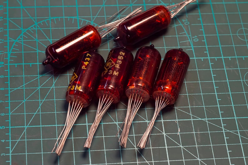 May include: Five red glass vacuum tubes with silver wires, labeled "P437" and "P352" on a green cutting mat.