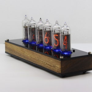 May include: A wooden clock with six clear glass Nixie tubes displaying the time as 16:54. The tubes have orange numbers and blue glow around the base.