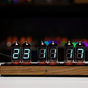 May include: A wooden base with six Nixie tubes displaying the time as 88:88:88. The tubes are lit with a bright blue-green light.