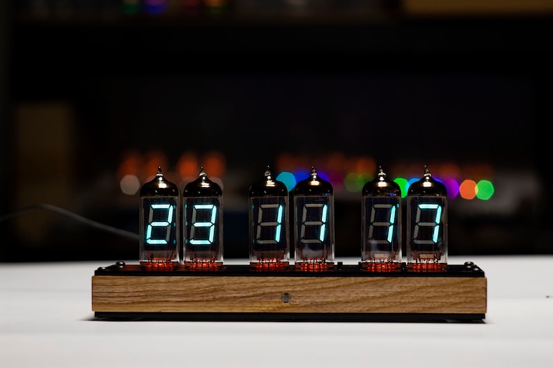 May include: A wooden base with six Nixie tubes displaying the time as 88:88:88. The tubes are lit with a bright blue-green light.