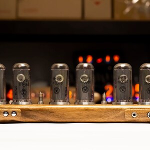 Puede incluir: Una base de madera con seis tubos de vac&iacute;o de vidrio transparente etiquetados "ИН-1Б 11 080". La base tiene dos conectores de audio en el lado derecho y cinco botones plateados en el lado izquierdo.