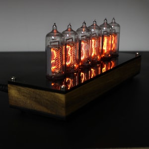 May include: A wooden clock with six glowing orange Nixie tubes displaying the time. The clock is on a black surface.