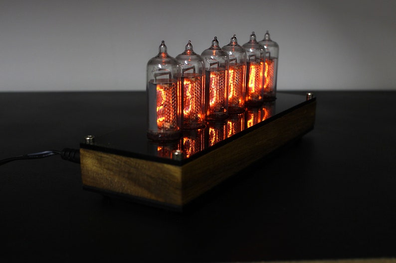 May include: A wooden clock with six glowing orange Nixie tubes displaying the time. The clock is on a black surface.