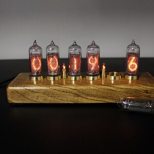 May include: A wooden clock with six glowing Nixie tubes displaying the time 01:19:06. The clock is on a black surface.