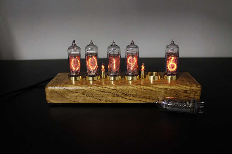 May include: A wooden clock with six glowing Nixie tubes displaying the time 01:19:06. The clock is on a black surface.