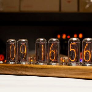 Puede incluir: Un reloj de madera con seis tubos Nixie que muestran la hora 09:16:56. Los tubos est&aacute;n iluminados con un brillo naranja.