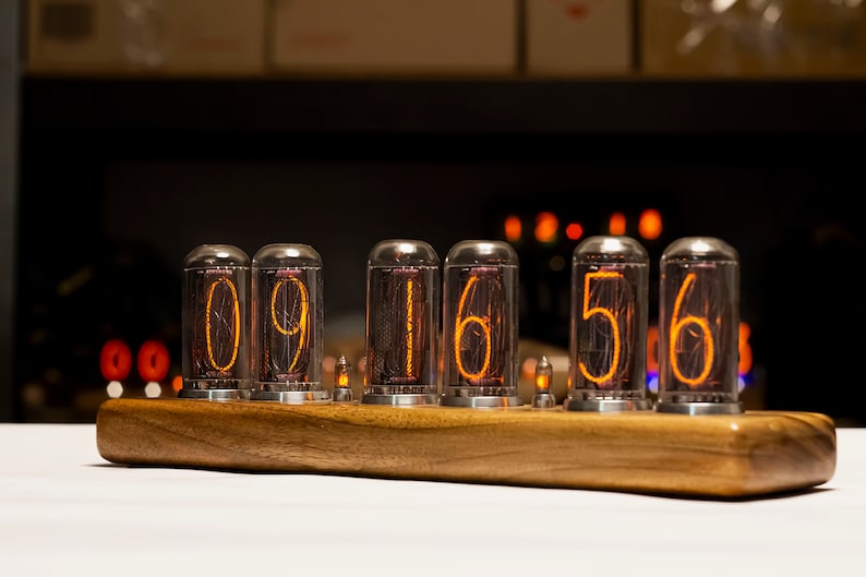 Puede incluir: Un reloj de madera con seis tubos Nixie que muestran la hora 09:16:56. Los tubos est&aacute;n iluminados con un brillo naranja.