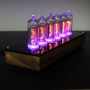 May include: A wooden clock with six glowing Nixie tubes displaying the time. The tubes are lit with a purple hue and the clock is sitting on a black surface.