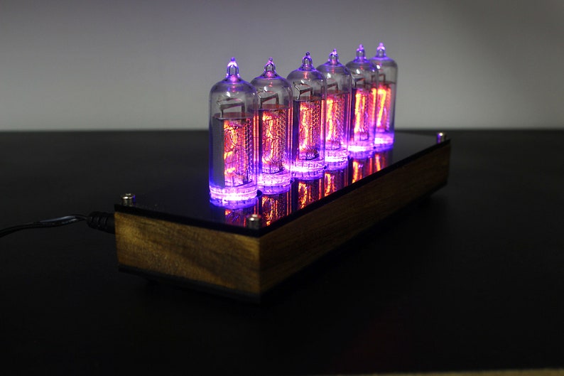 May include: A wooden clock with six glowing Nixie tubes displaying the time. The tubes are lit with a purple hue and the clock is sitting on a black surface.