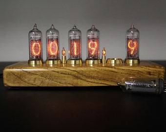 May include: A nixie tube clock featuring five vertical glass vacuum tubes with glowing orange numerical displays mounted on a rectangular wooden base with brass accents, accompanied by an additional unlit glass tube lying horizontally.