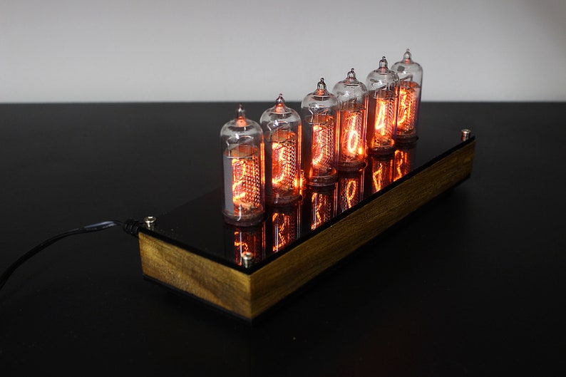 May include: A wooden clock with six glowing Nixie tubes displaying the time. The clock is on a black surface.