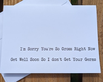 May include: A white greeting card and envelope set with the text "I'm Sorry You're So Gross Right Now Get Well Soon So I don't Get Your Germs". The card is on a wooden surface.