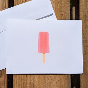 May include: A white card with a pink popsicle on a wooden background.
