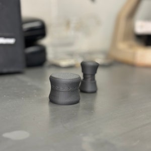 May include: Two black, cylindrical containers with a textured surface. The larger container has a pattern of arrows around the middle.