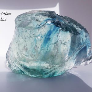 Può includere: Un grande cristallo di Andara blu e verde traslucido con una texture naturale ruvida. Il cristallo è etichettato "Ultra Rare Andara".