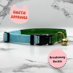 May include: A light blue and green cat collar with a breakaway buckle and a gold bell. The collar has the text "Swiftie Approved" on a pink cat-shaped tag.