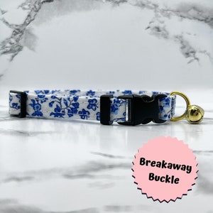 May include: White and blue floral patterned cat collar with a black breakaway buckle and a gold bell.