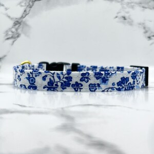 May include: A white and blue floral patterned dog collar with a gold buckle and black adjustable buckle.