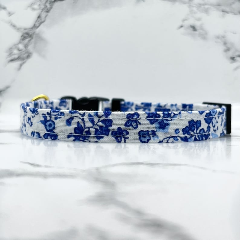 May include: A white and blue floral patterned dog collar with a gold buckle and black adjustable buckle.