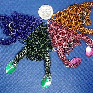May include: Five small triangular chainmail ornaments in different colours: purple, green, pink, orange, and silver. Each ornament has a teardrop-shaped pendant at the bottom.