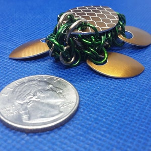 May include: A green and gold metal turtle sculpture with a textured shell. The turtle is about the size of a US quarter.