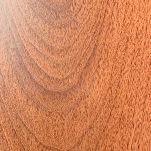 May include: Close-up of a wood grain pattern with a reddish-brown color. The grain is swirling and has a natural, organic look.