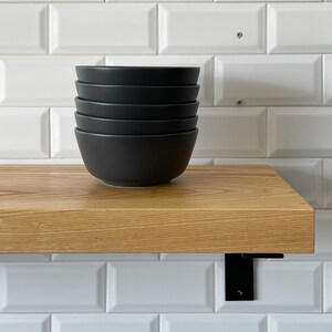 May include: A stack of five black ceramic bowls on a wooden shelf with black metal brackets.