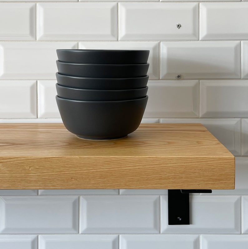 May include: A stack of five black ceramic bowls on a wooden shelf with black metal brackets.
