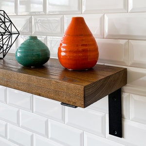 May include: A wooden shelf with black metal brackets, holding two ceramic vases. The vase on the left is teal green and the vase on the right is orange.
