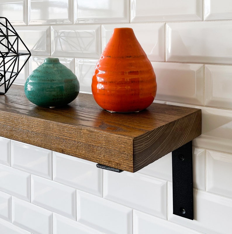 May include: A wooden shelf with black metal brackets, holding two ceramic vases. The vase on the left is teal green and the vase on the right is orange.