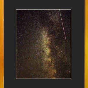 Peut inclure: Une impression photographique rectangulaire montrant un ciel nocturne étoilé avec la bande de la Voie lactée, encadrée par un passe-partout noir épais. Une fine traînée blanche brillante représentant un météore traverse le coin supérieur droit.