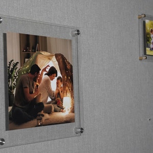 May include: A framed photograph of a family of three inside a tent-like structure. The father is sitting on the floor, the mother is sitting next to him, and the child is sitting in front of them. The photo is lit with warm, string lights.