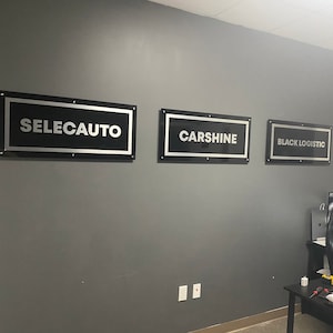 May include: Three black and silver rectangular signs with white text on a gray wall. The signs read "SELECAUTO", "CARSHINE", and "BLACK LOGISTIC".