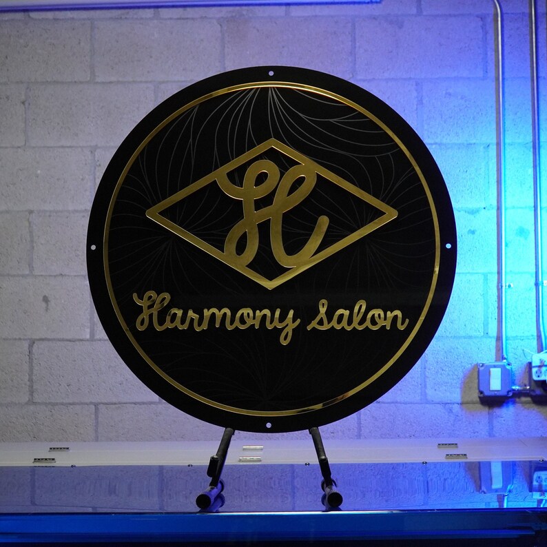 May include: A black circular sign with a gold diamond shape containing the letters "HC" and the text "Harmony Salon" in gold lettering.