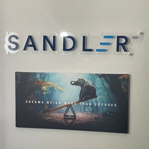 May include: A motivational quote, "Dreams weigh more than excuses", is printed on a canvas print featuring an elephant on a seesaw in a misty forest.