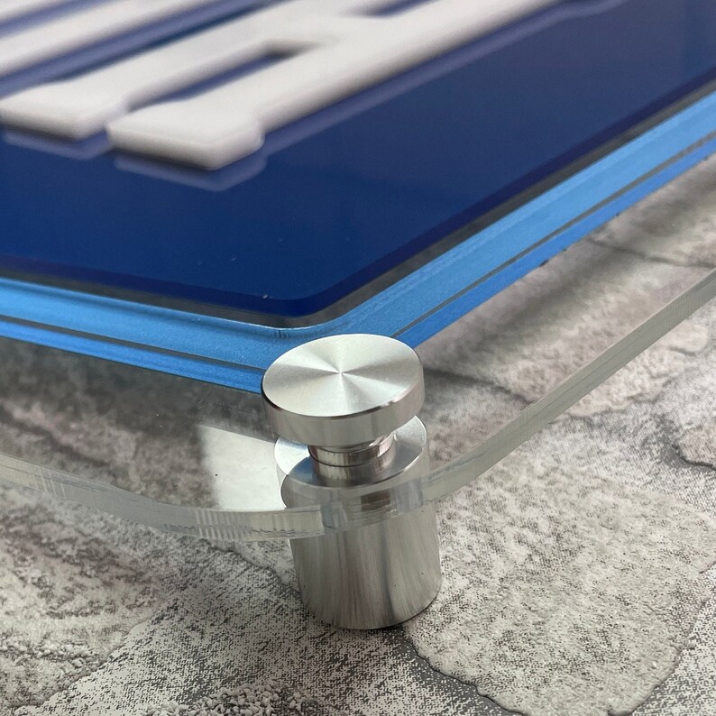 May include: Close-up of a silver metal stand with a round top and a cylindrical base. The stand is attached to a clear acrylic surface.