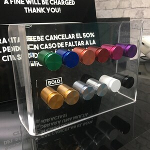 May include: A clear acrylic display case with a variety of colored and silver round knobs. The knobs are arranged in rows and are labeled with the word "BOLD".