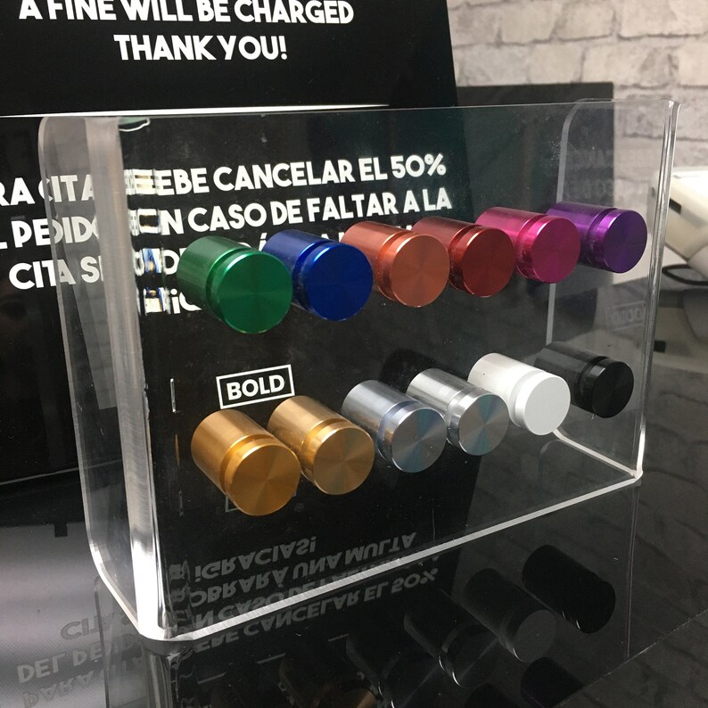May include: A clear acrylic display case with a variety of colored and silver round knobs. The knobs are arranged in rows and are labeled with the word "BOLD".