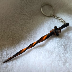May include: A black and orange twisted metal keychain with a silver key ring. The keychain is shaped like a sword.