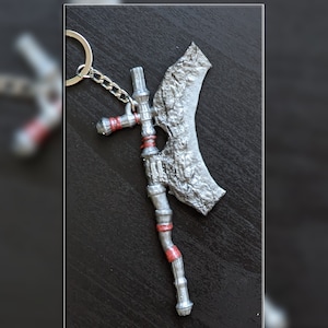 May include: A silver-colored axe keychain with red accents. The axe has a curved blade and a detailed handle.