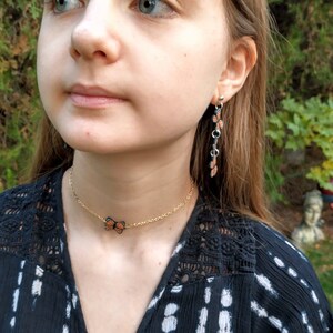 May include: A gold-colored chain necklace with a butterfly pendant and matching dangling earrings. The butterfly pendant and earrings feature orange and black details. The jewelry is worn against a dark patterned top.